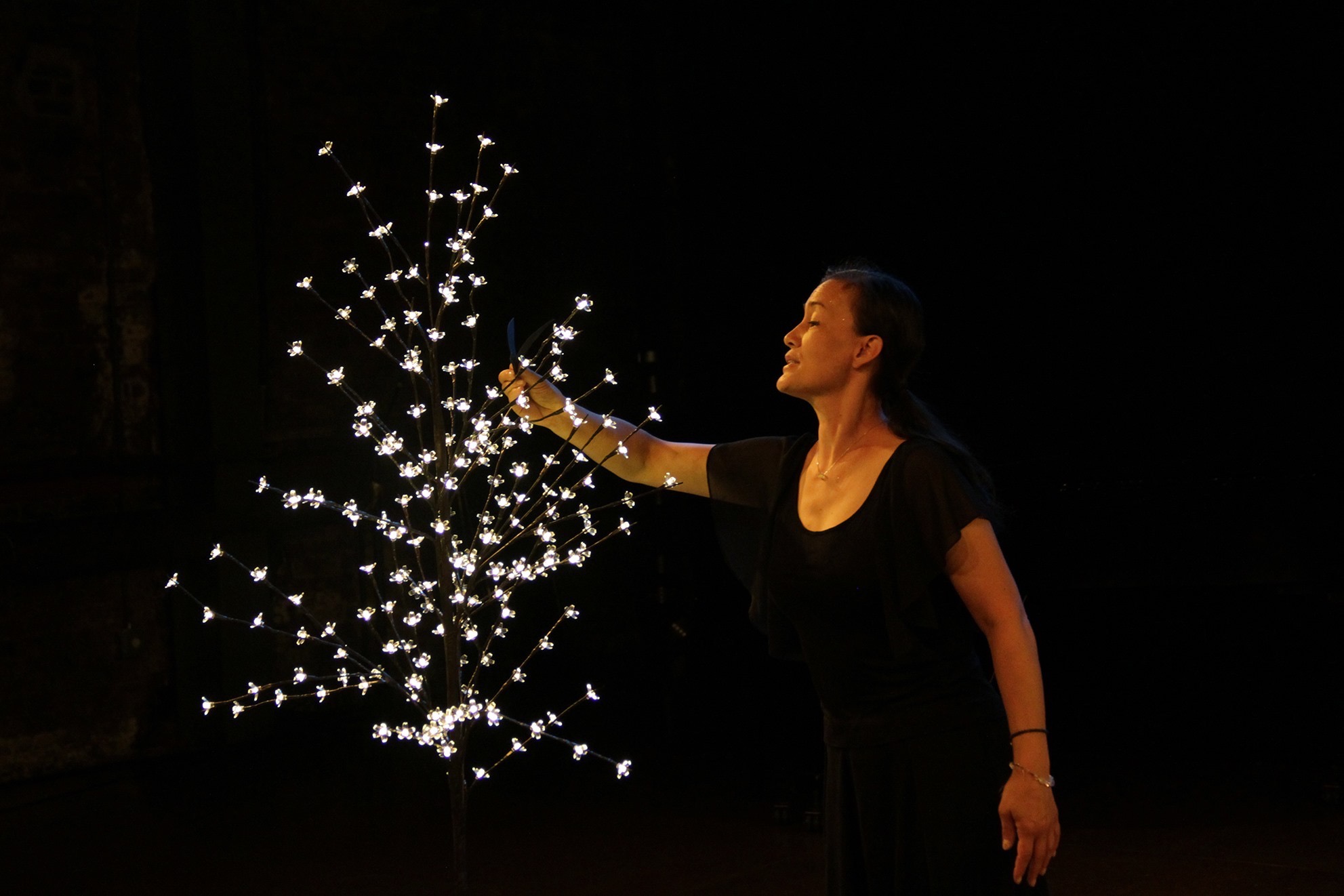 A woman of color dressed in black with a serene look on her face turns to a constellation of small white lights